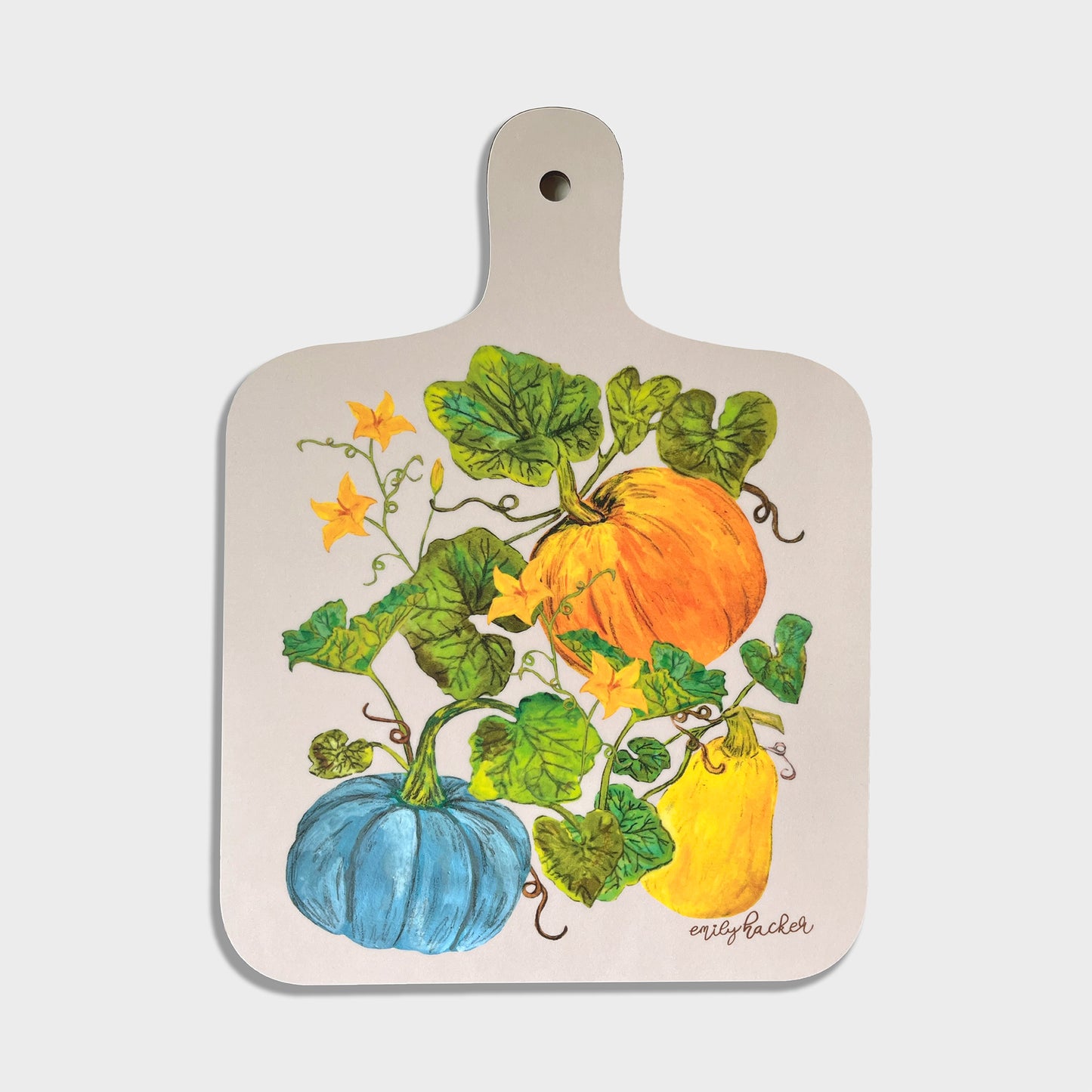 A small chopping board with a handle, featuring hand-painted illustrations of pumpkins, squash, and leaves in colorful colors on a light cream background.