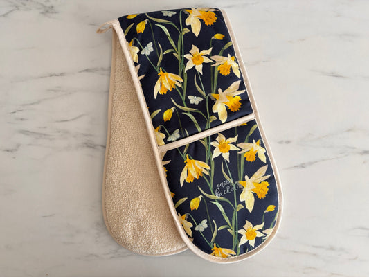 Double oven glove with hand painted wild daffodils on a dark background placed on a marble worktop