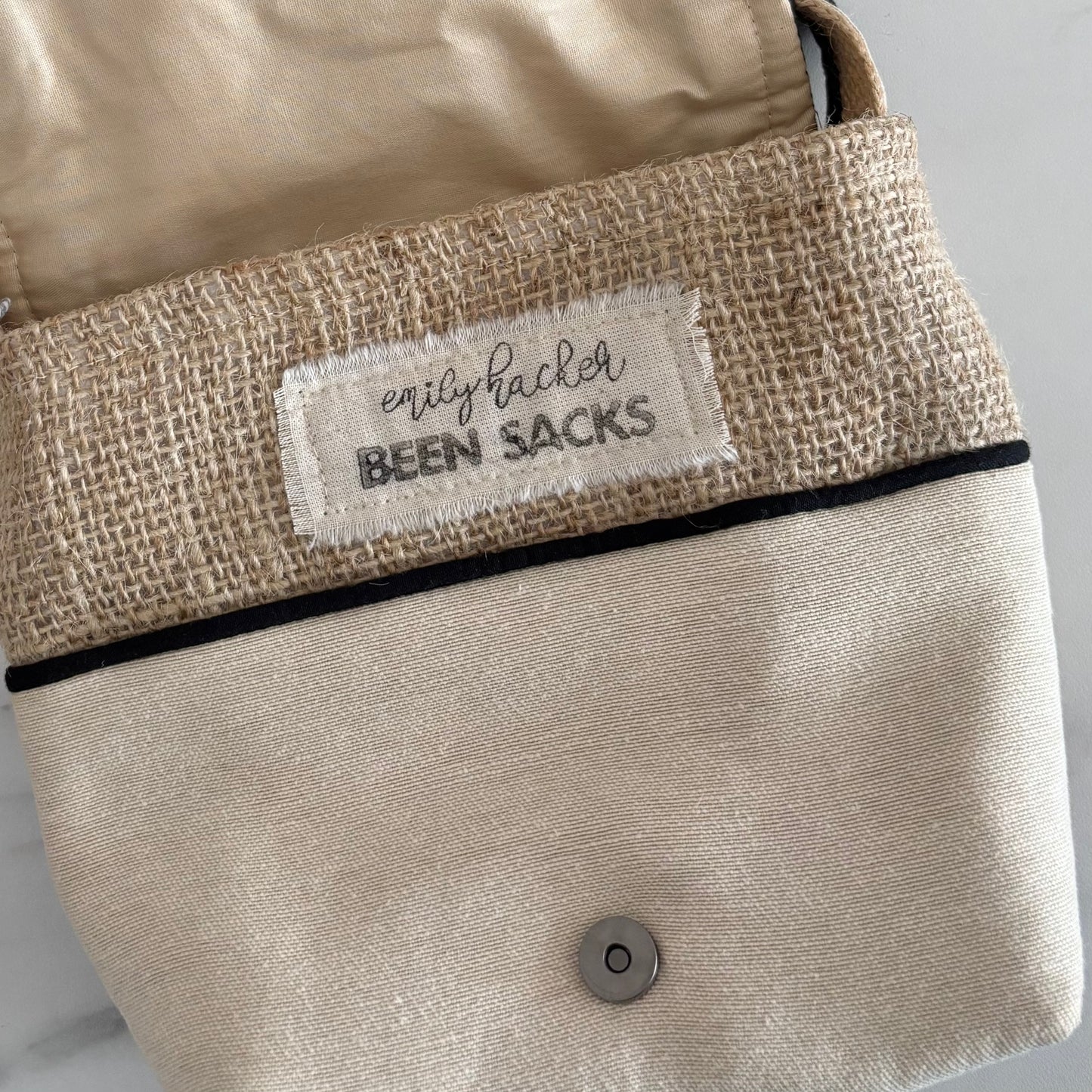 Beige bag with a label reading 'emily hacker BEEN SACKS' on a neutral background