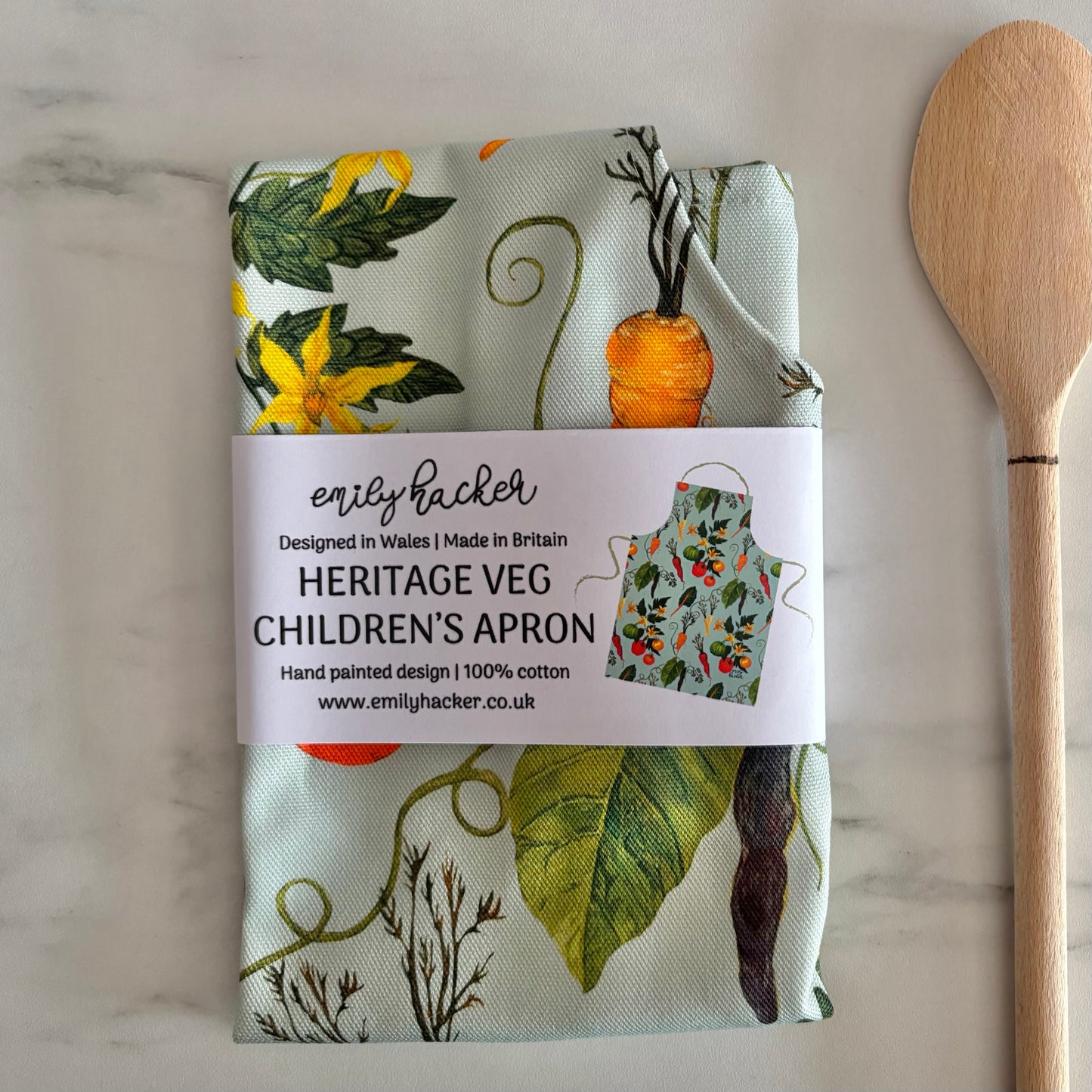 Eco friendly children's apron with vegetable pattern and wooden spoon on marble surface wrapped in a belly band