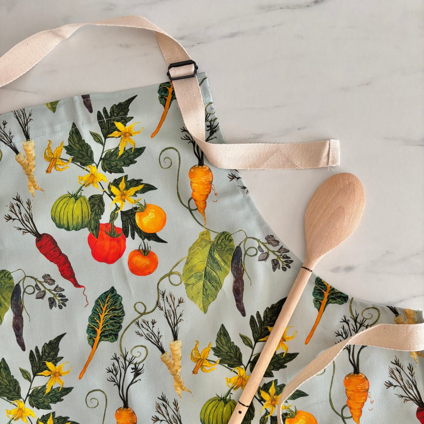Colorful apron with vegetable pattern and wooden spoon on marble surface
