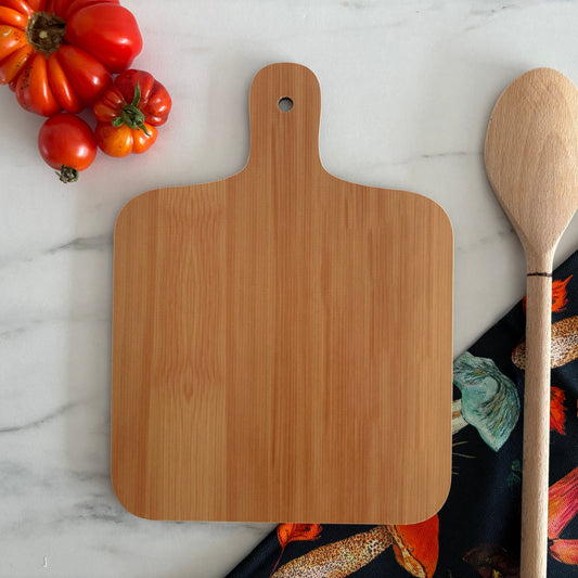 Wooden cutting board and spoon on a marble surface with tomatoes and a mushroom pattern tea towel