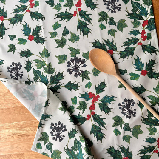 Holly and ivy leaf patterned tea towel with wooden spoon on an oak countryside home table