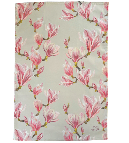 A cotton tea towel with hand painted magnolia bloom illustrations, predominantly pink and green in color.
