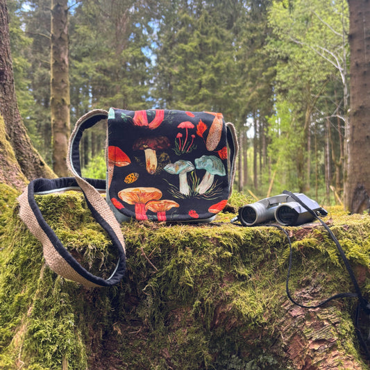 Woodland mushroom patterned bag and binoculars on a mossy log in a forest setting