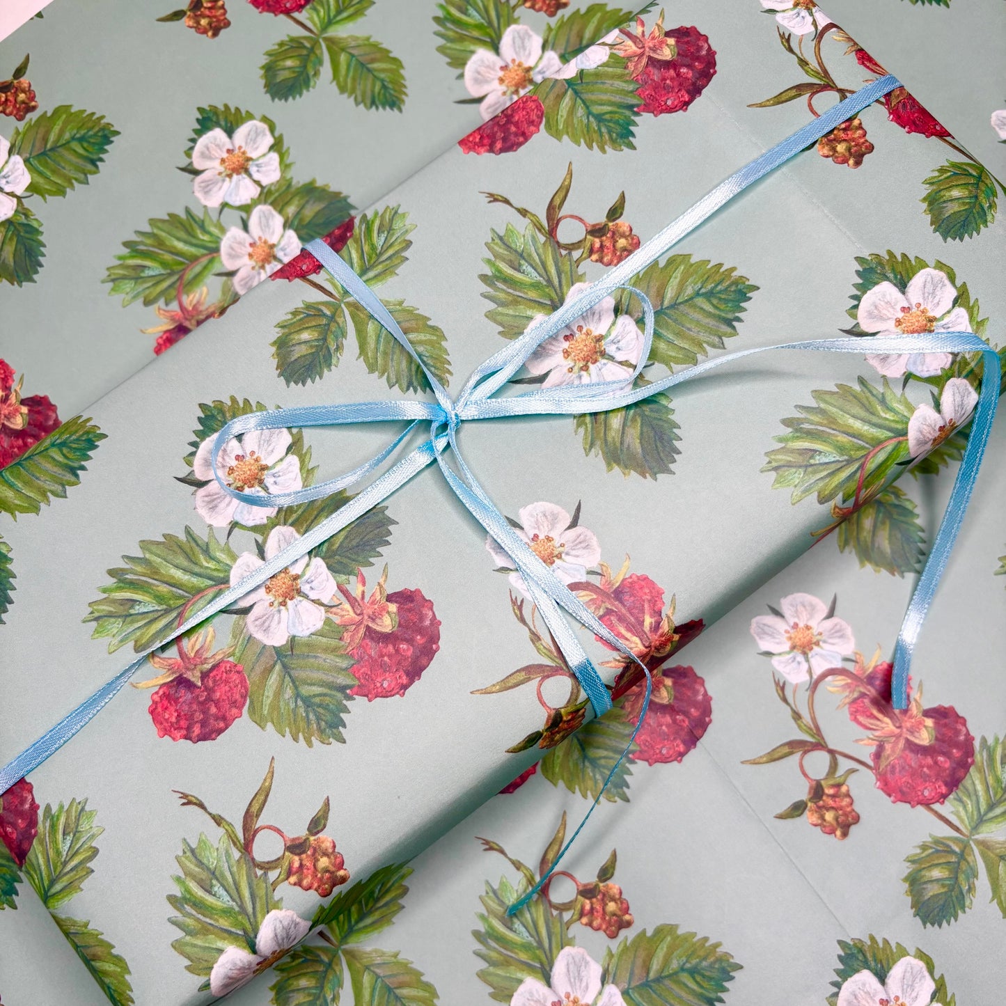 Strawberry Gift wrapped with wild strawberry floral patterned paper with a blue ribbon on a matching background