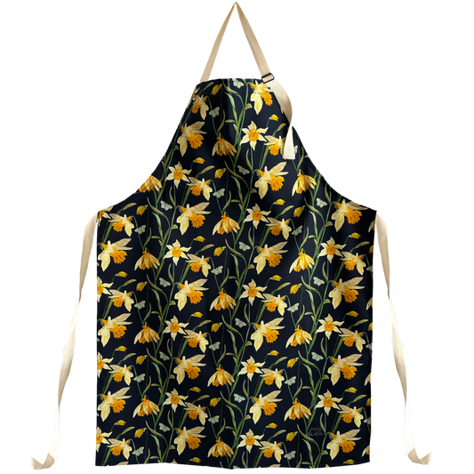 An apron featuring a hand painted design with daffodil blooms and buds in yellow on a navy background, with adjustable neck and waist ties.