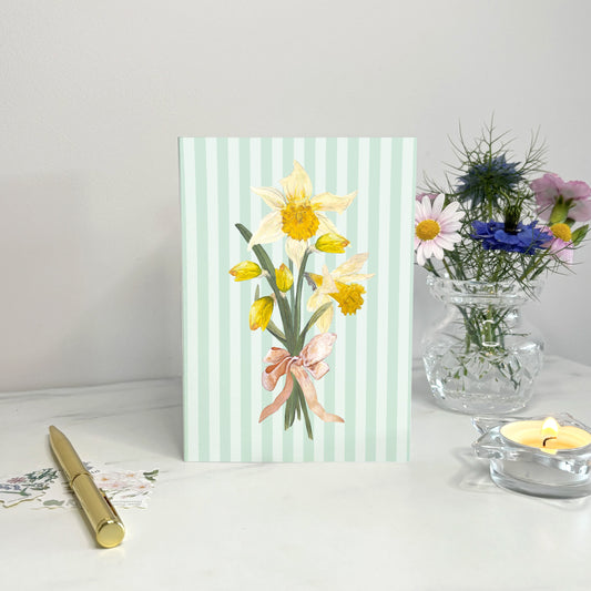 Daffodil Hand illustrated card with spring floral design on a white surface with a candle and flowers in the background