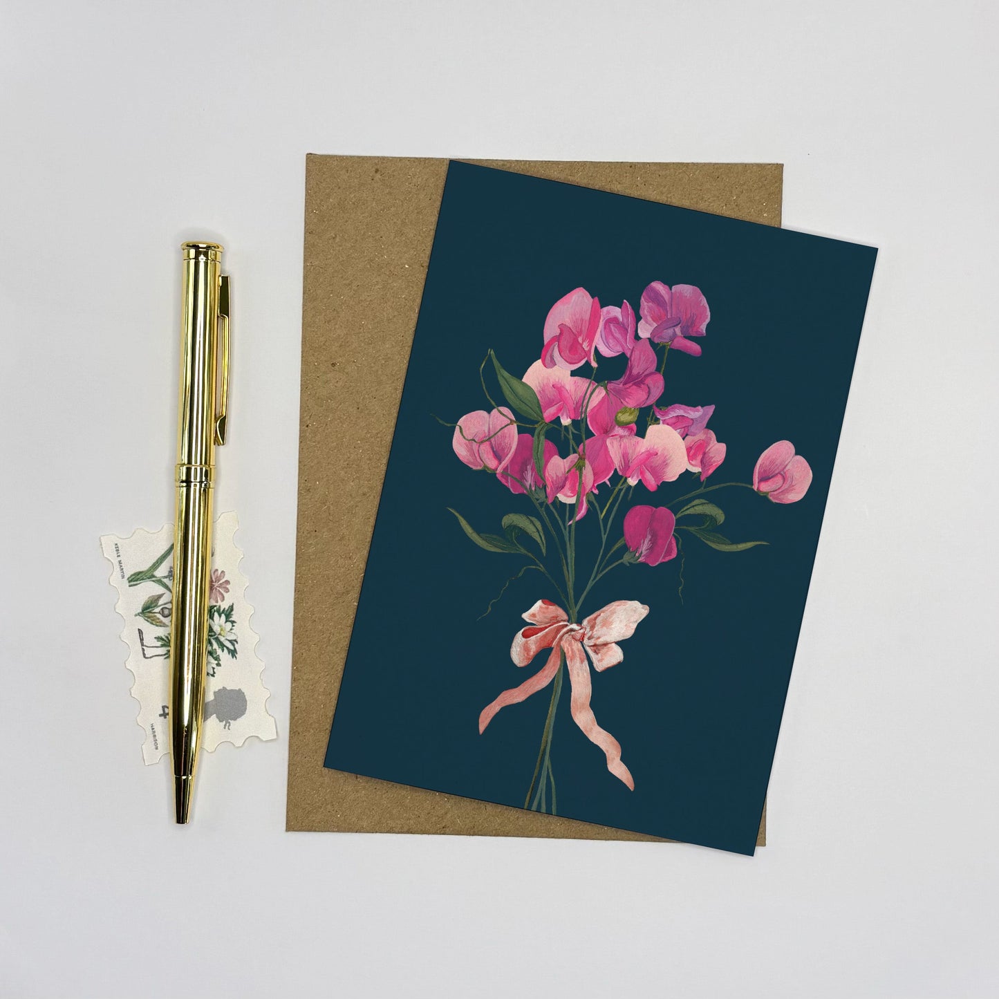 Sweet pea Greeting card with pink floral design on a dark blue background, accompanied by a pen and decorative stickers.