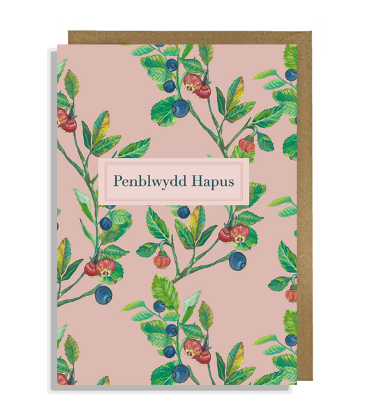 Welsh Happy Birthday card with hand painted illustrations of bilberry fruit, flowers and leaves on a pink background.