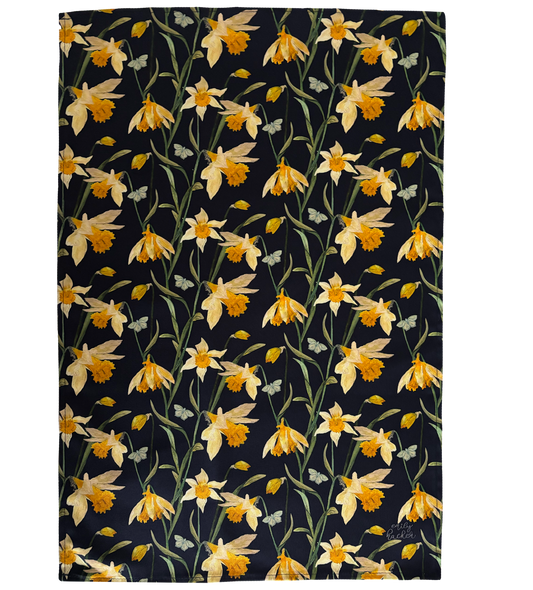 A cotton tea towel with hand painted illustrations of wild daffodils in vibrant colours on a dark background.