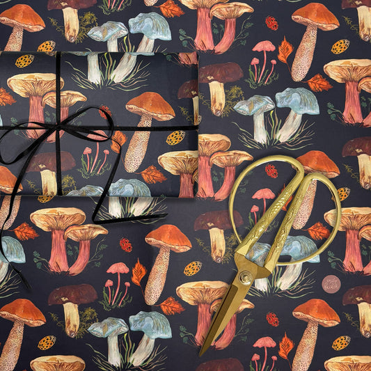 Woodland mushroom Gift gift wrap with hand painted mushroom illustrations of boletes, field blewitt and toadstools next to gold scissors on a matching background