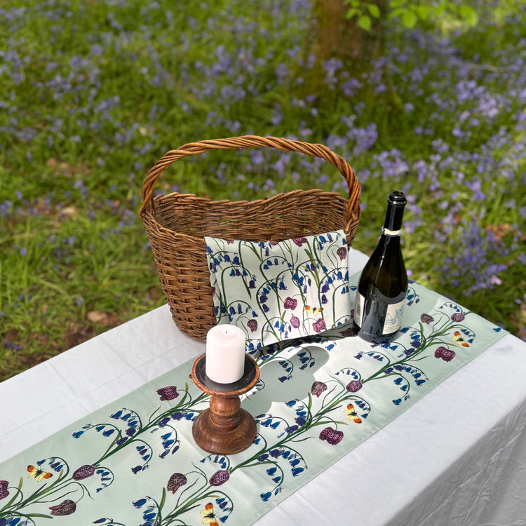 Bluebell and snakehead fritillary design cotton tea towel and wildflower cotton table runner on a table against a bluebell woods background