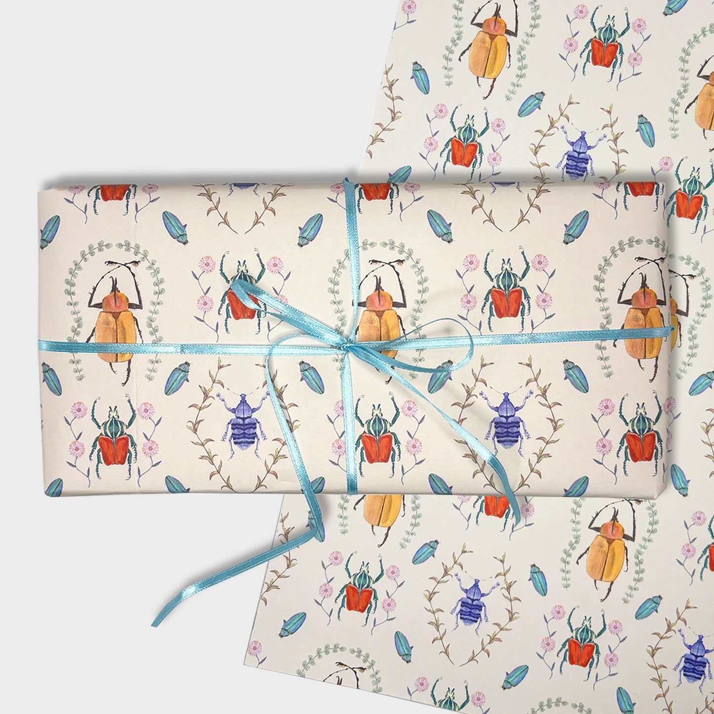 Beetle Gift wrapped in hand illustrated beetle collector patterned paper with a blue ribbon on a white background
