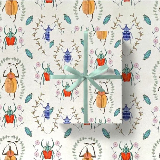 Gift wrap with a blue ribbon on a cream background featuring jewel coloured beetles and foliage.