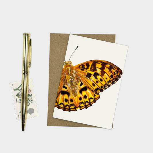 A7 greeting card of a yellow and black high brown fritillary butterfly on a white card, layered over a brown kraft envelope, styled on a light gray background next to a gold pen and a small decorative sticker.
