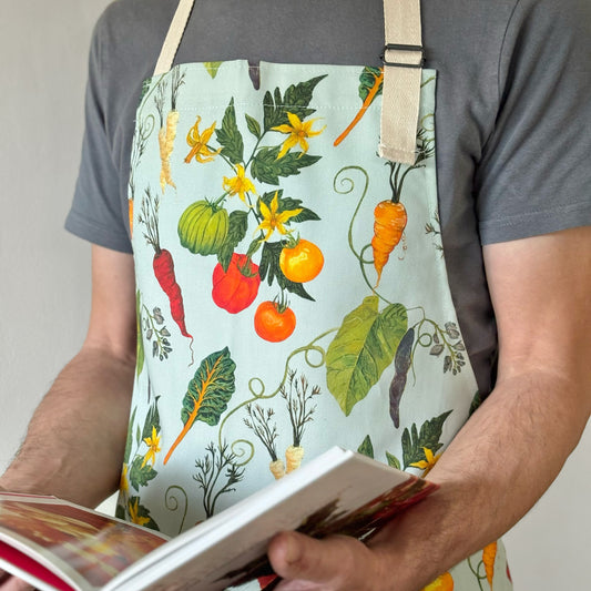 Person wearing a colorful apron with vegetable carrot tomato and bean pattern, holding a book.