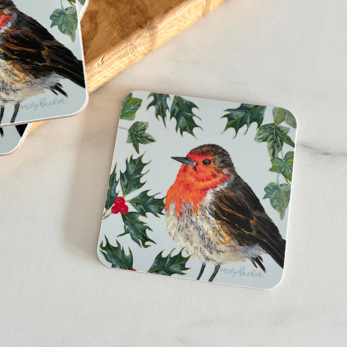 Melamine coaster featuring hand painted winter scene of green Holly and ivy leaves illustration, with a robin on a light blue background.
