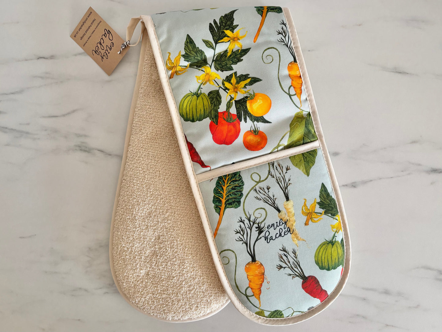 Pair of oven mitts with heritage vegetable tomatoes bean chard and carrot pattern on a marble surface