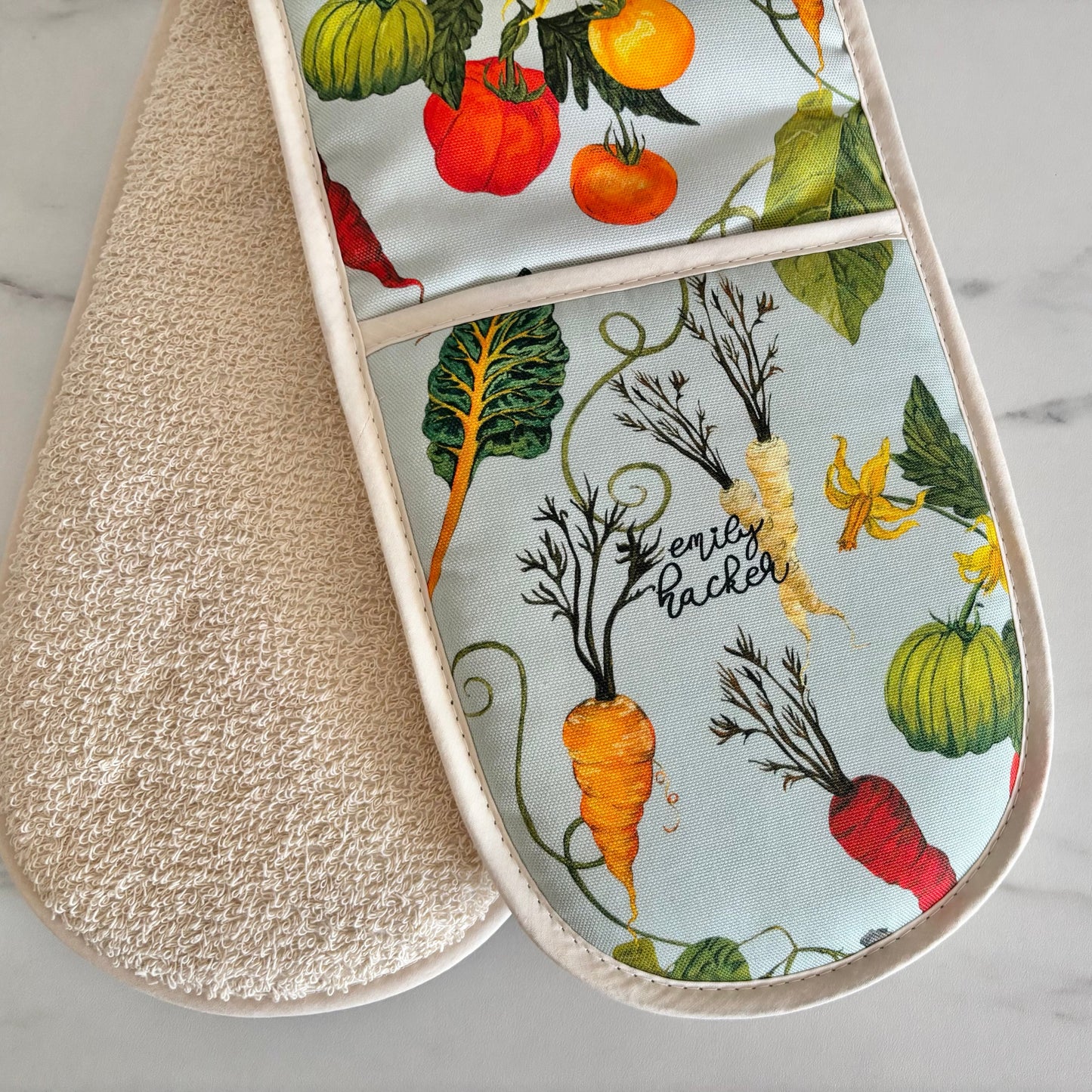 Double oven mitt with heritage vegetable pattern and light blue background on a marble surface