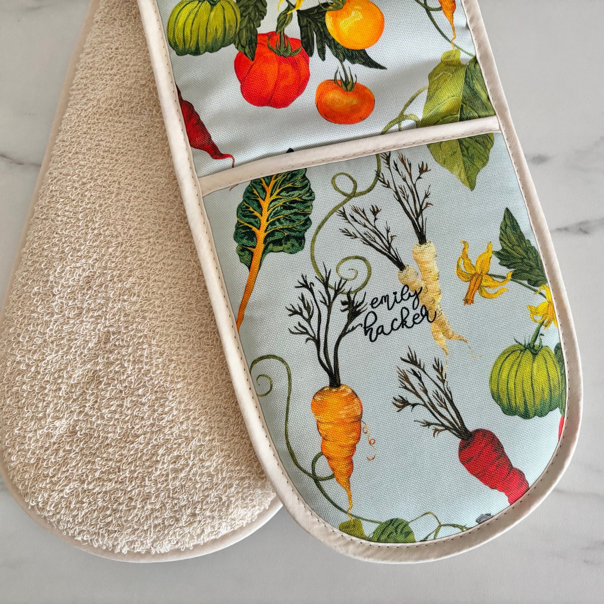 Double oven mitt with heritage vegetable pattern and light blue background on a marble surface