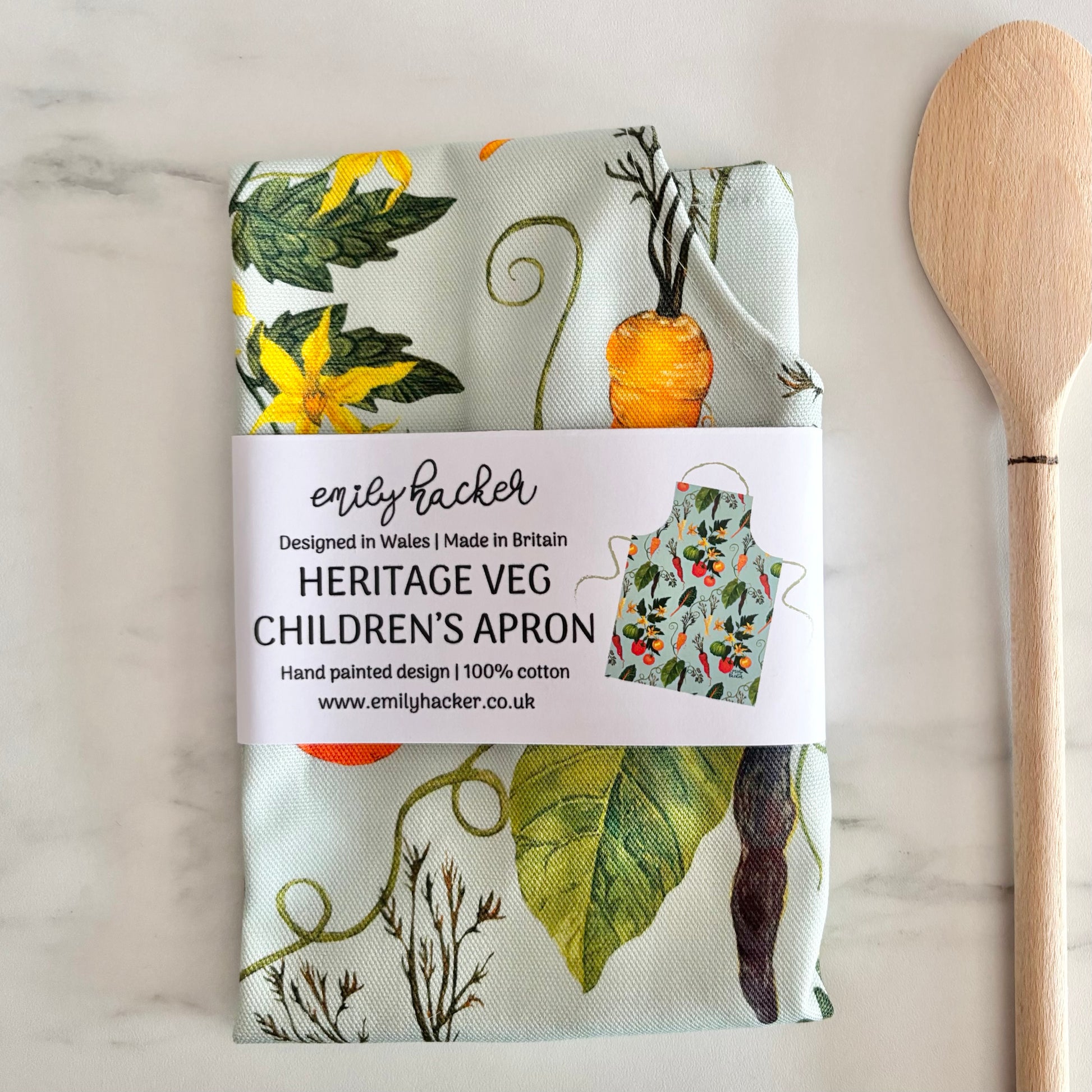 Cotton children's apron with vegetable pattern and wooden spoon on marble  surface wrapped in a belly band