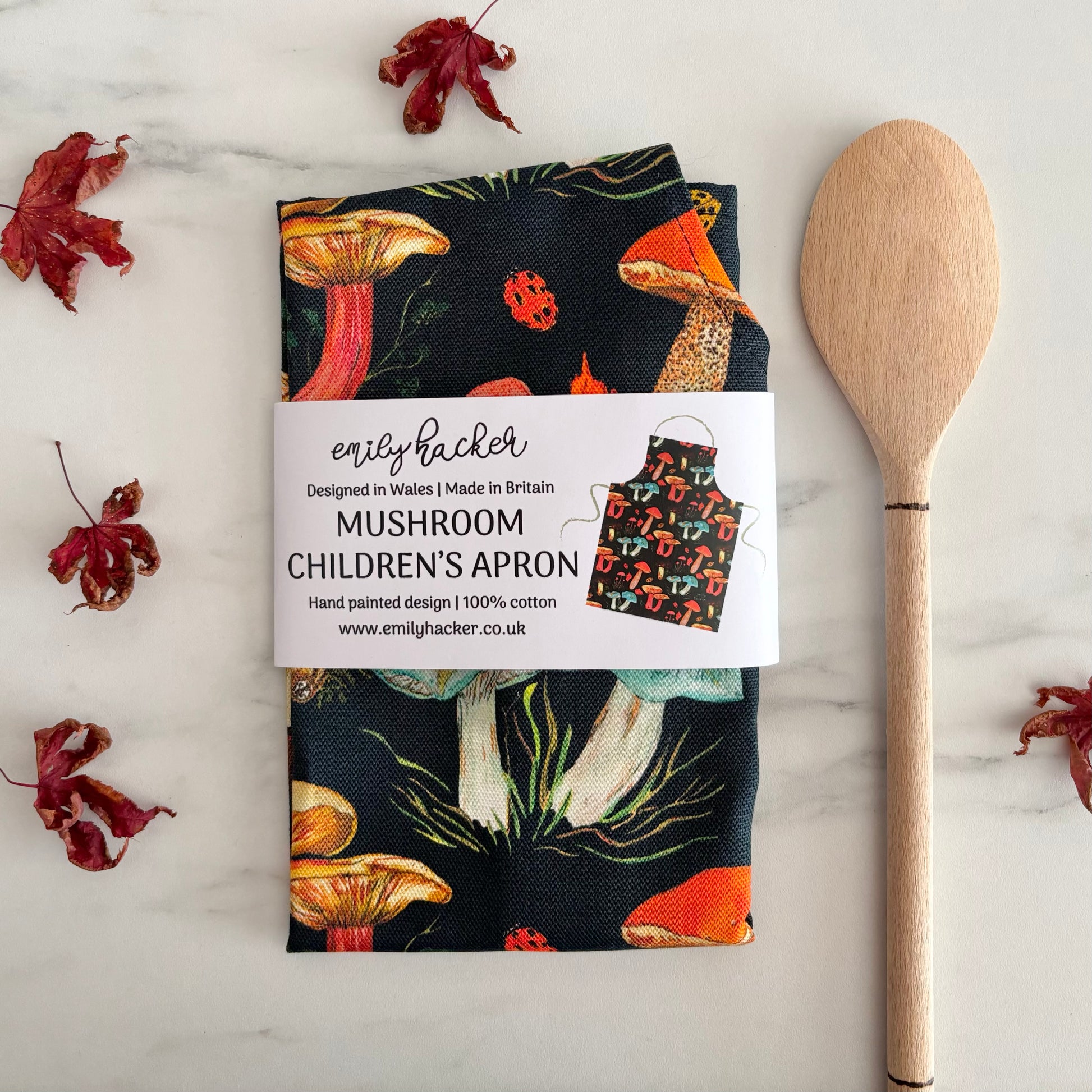 Children’s cotton apron with autumn mushroom design packaged in sustainable paper bellyband
