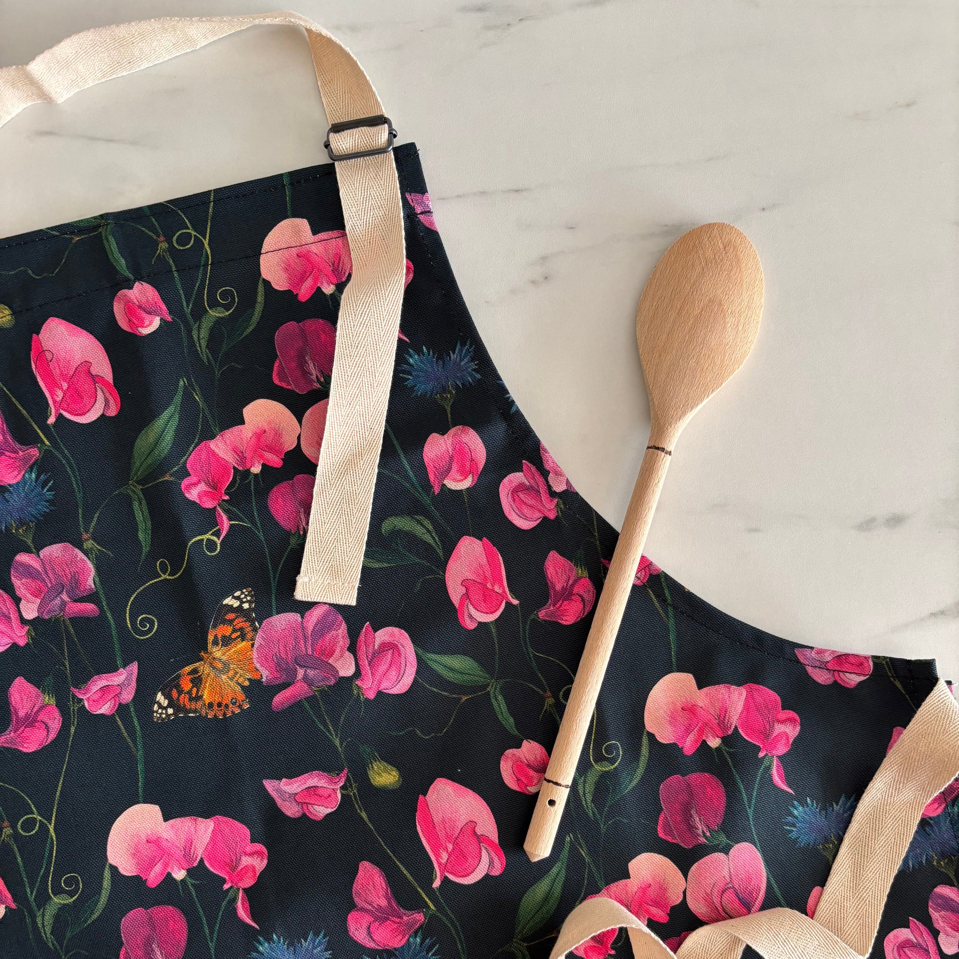 Floral apron with pink sweet pea flowers and a wooden spoon on a light background