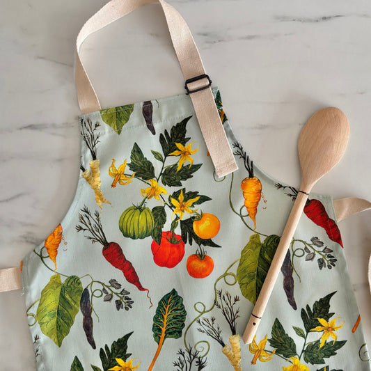 Kids apron with vegetable pattern and wooden spoon on marble surface