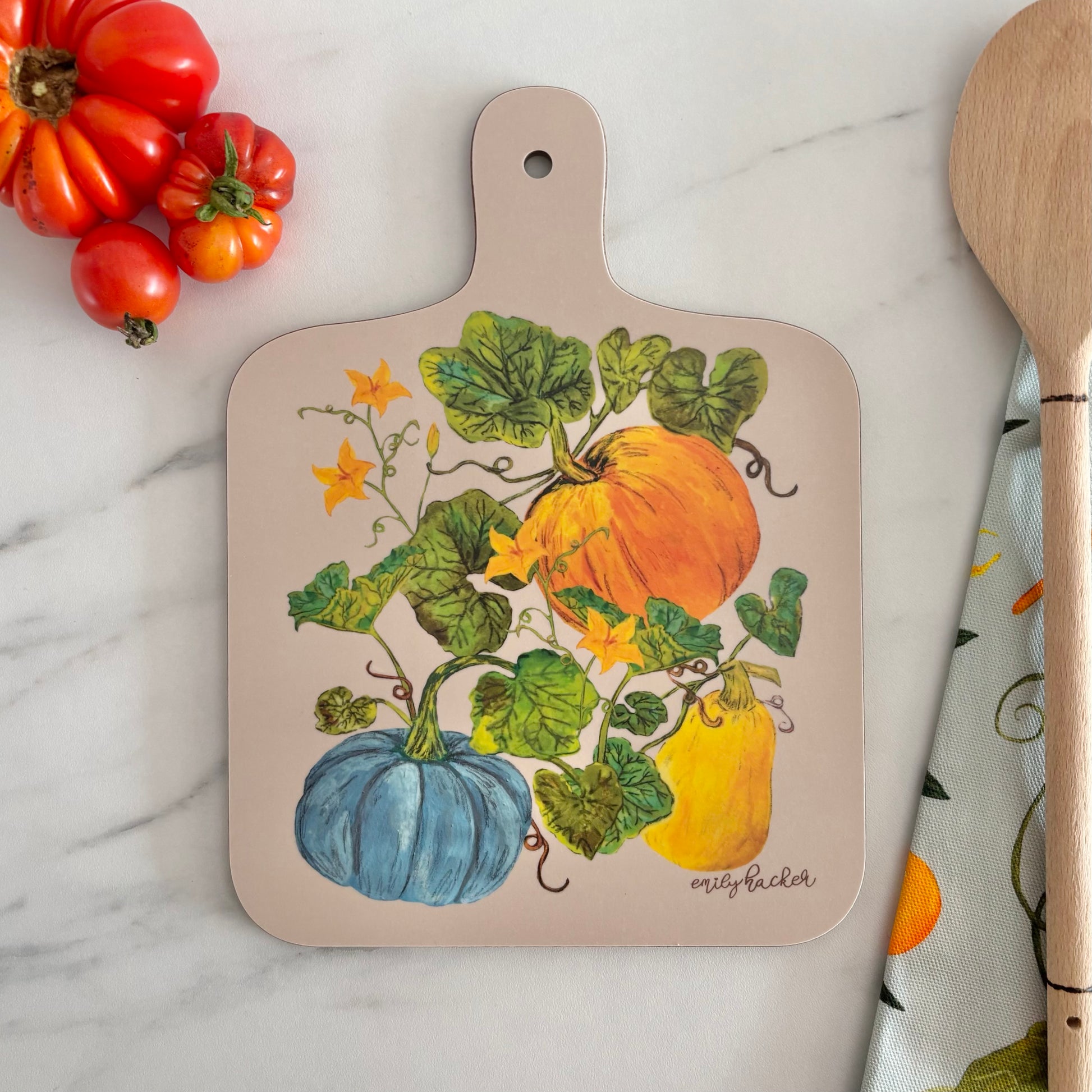 Pumpkin Melamine study chopping board or charcuterie board decorated with hand painted orange pumpkin blue heritage and yellow squash illustrations the board is photographed next to tomatoes and a wooden spoon