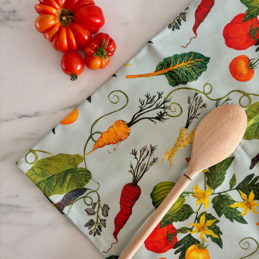 Fabric with vegetable pattern, wooden spoon, and tomatoes on a marble surface