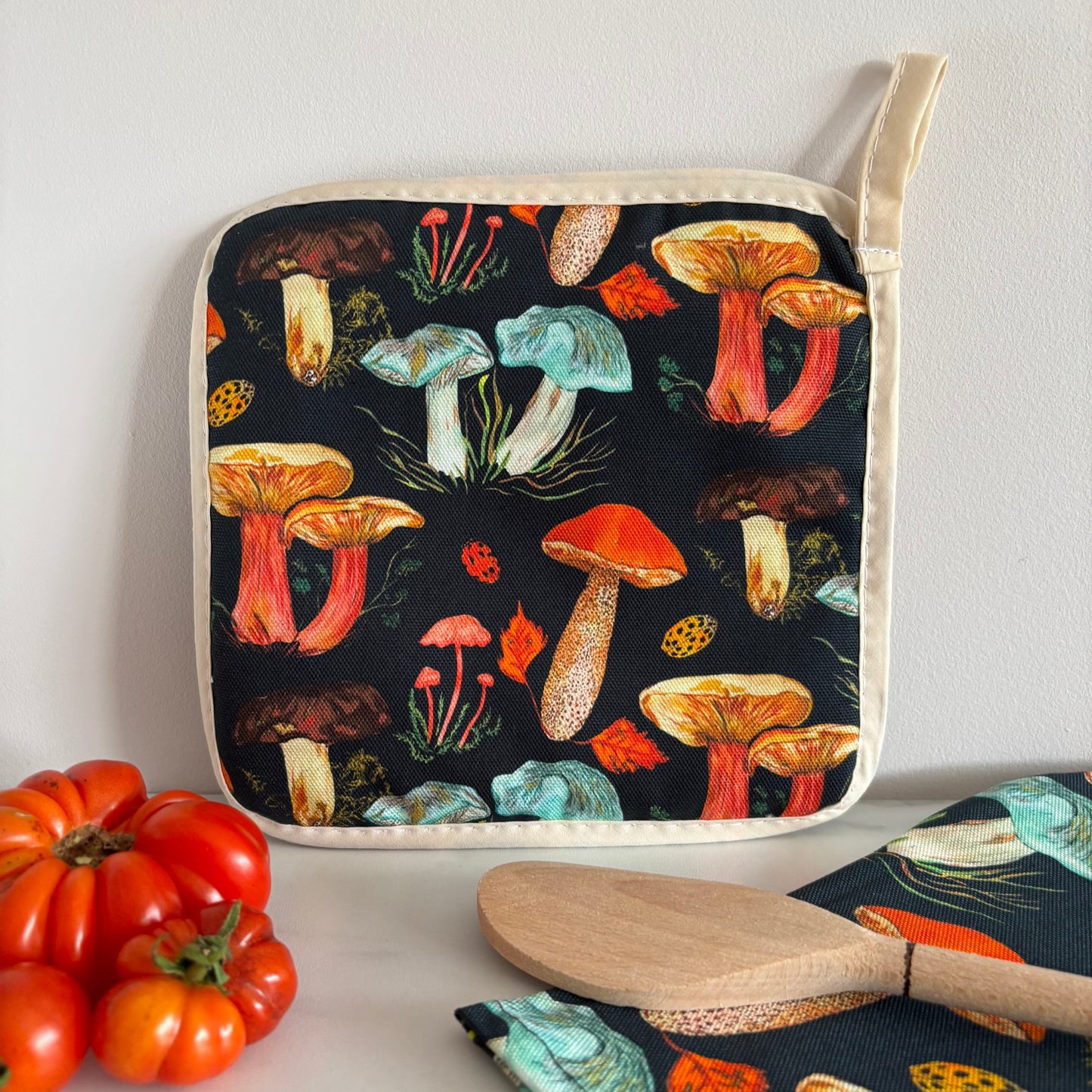 Potgrab featuring black background and woodland mushroom pattern next to wooden spoon and tomatoes