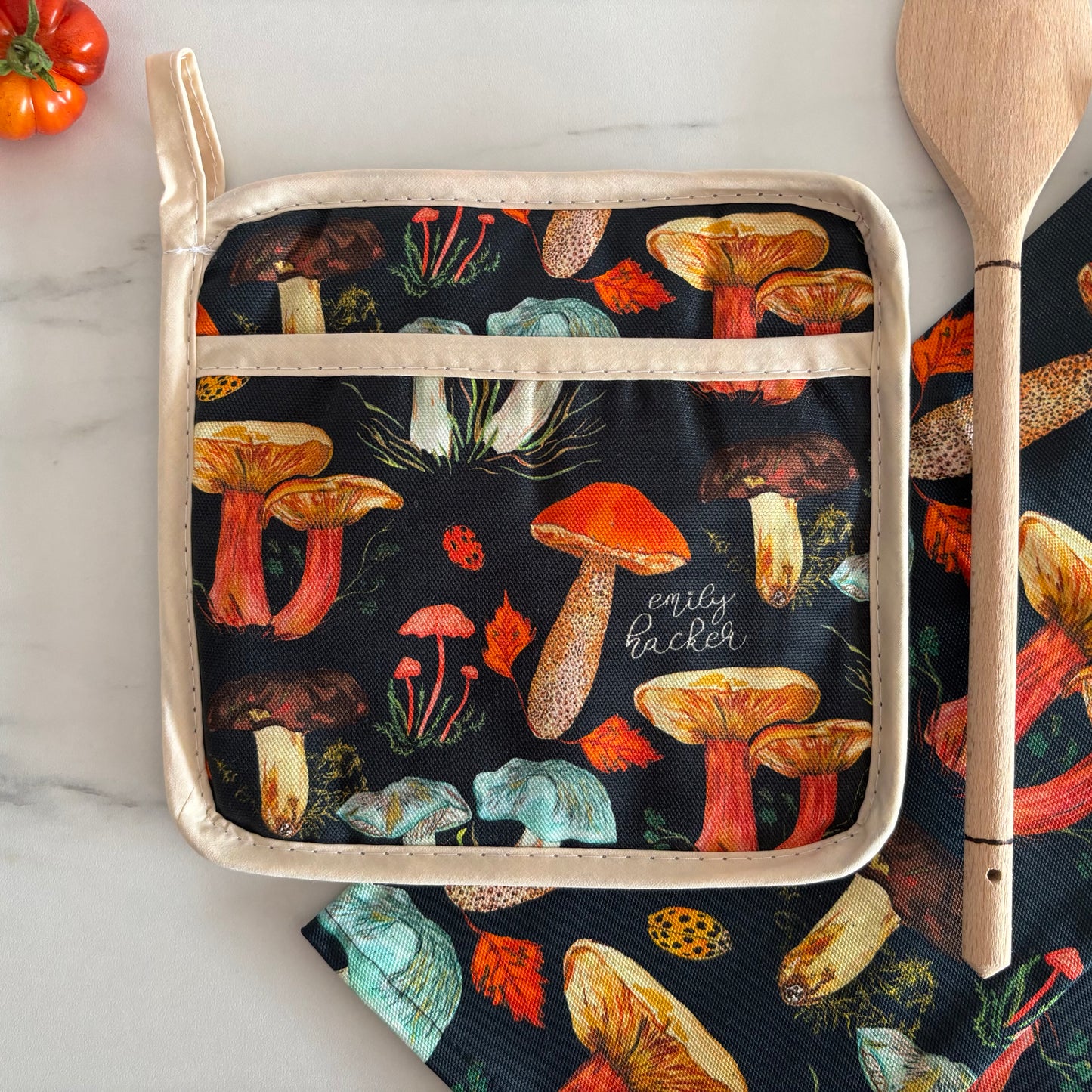 Potgrab featuring black background and woodland mushroom pattern next to wooden spoon and tomatoes