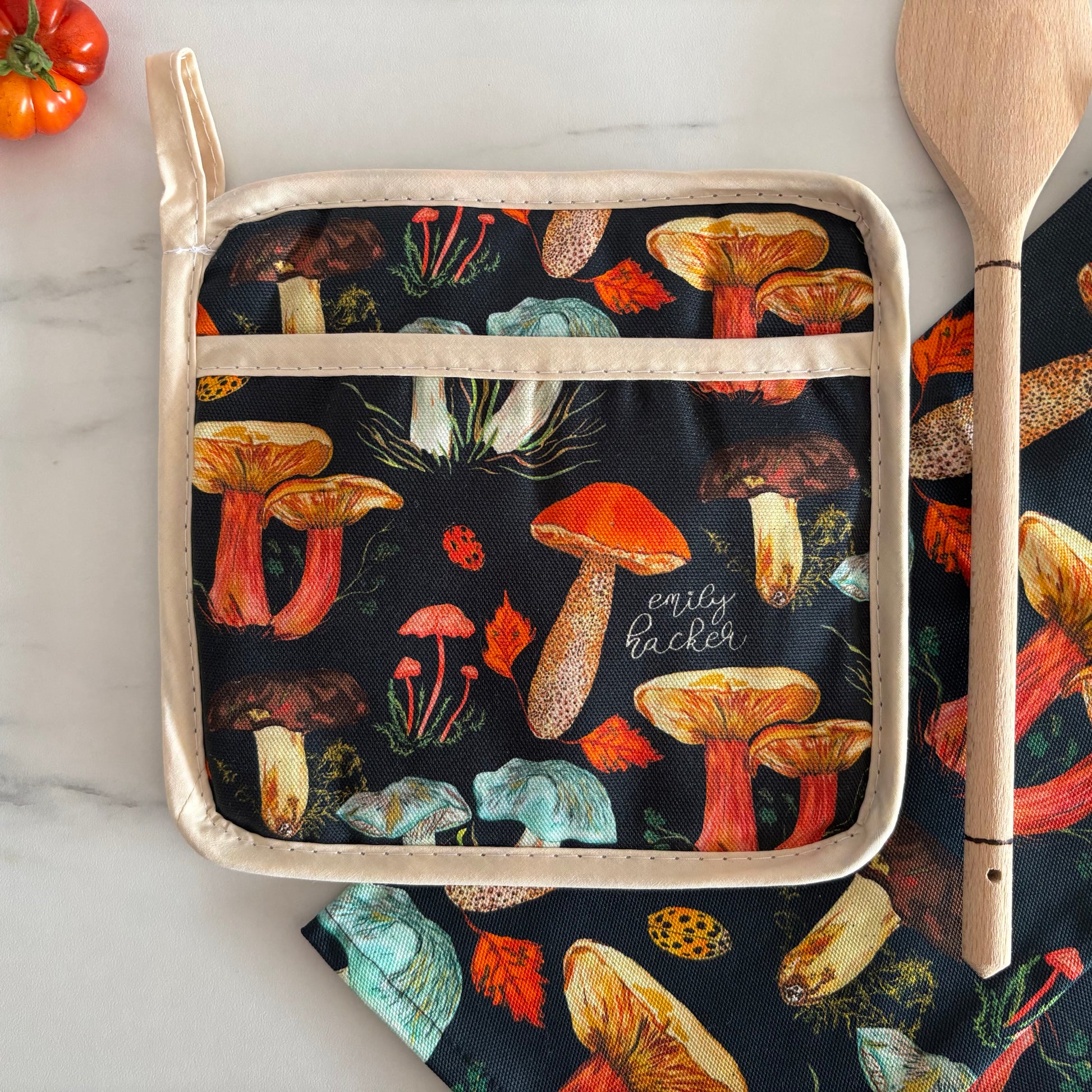 Potgrab featuring black background and woodland mushroom pattern next to wooden spoon and tomatoes