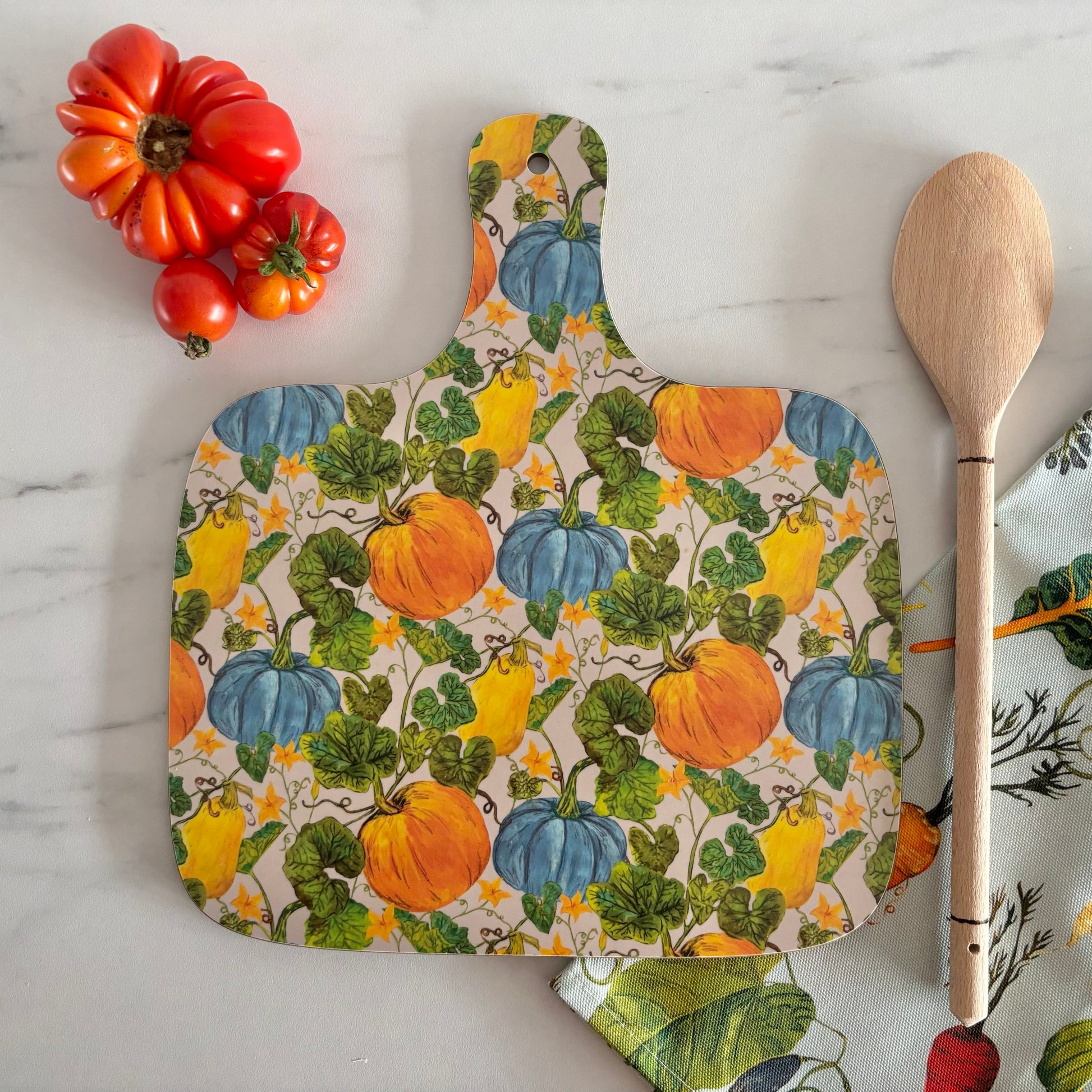  chopping and cutting board with pumpkin pattern on a marble surface with tomatoes and a wooden spoon.