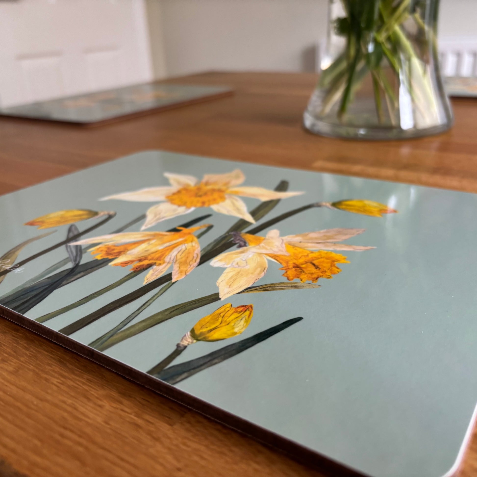 Placemat with wild daffodil floral design on a wooden table next to a vase of pink flowers