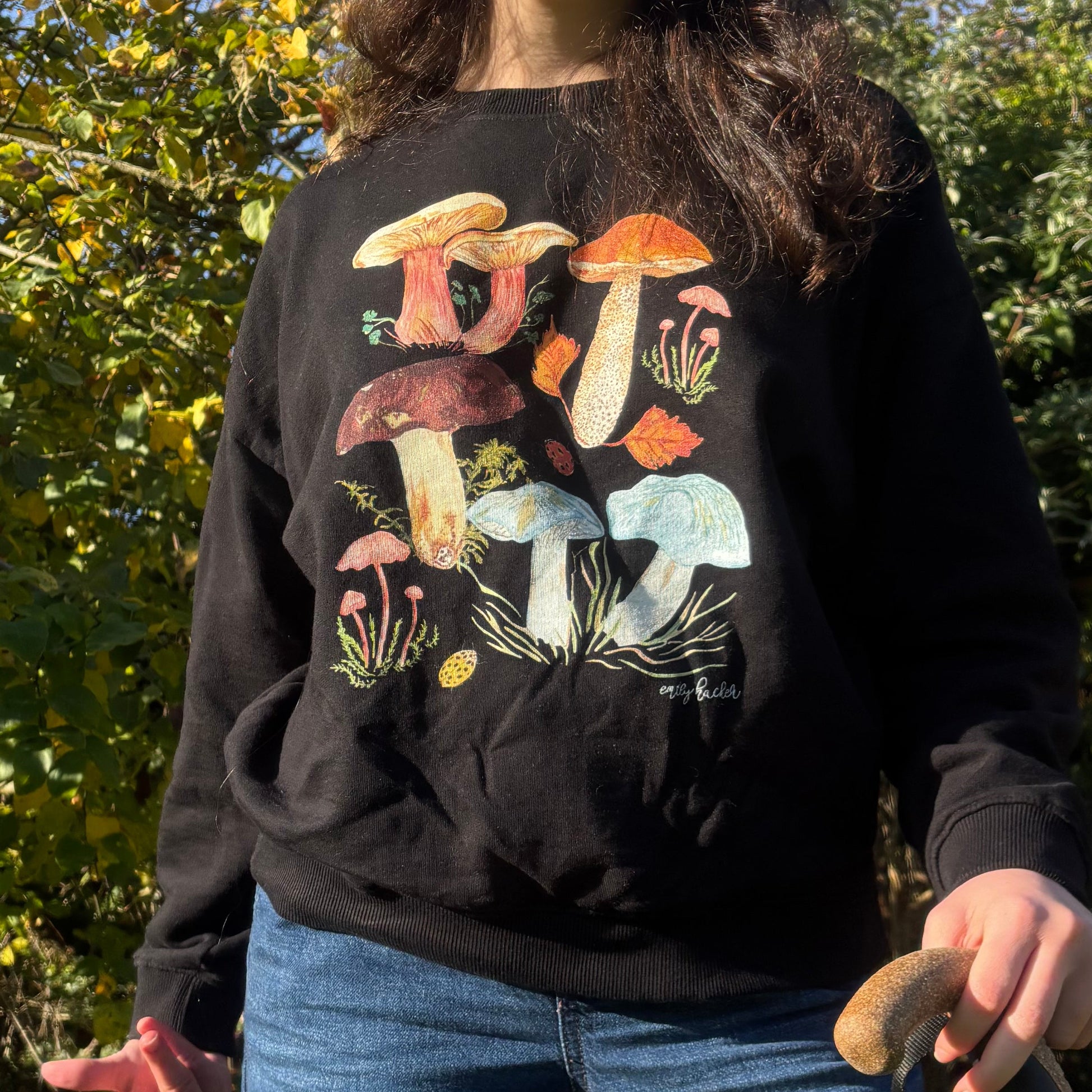 Person wearing a black organic cotton sweatshirt with colorful toadstool designs outdoors