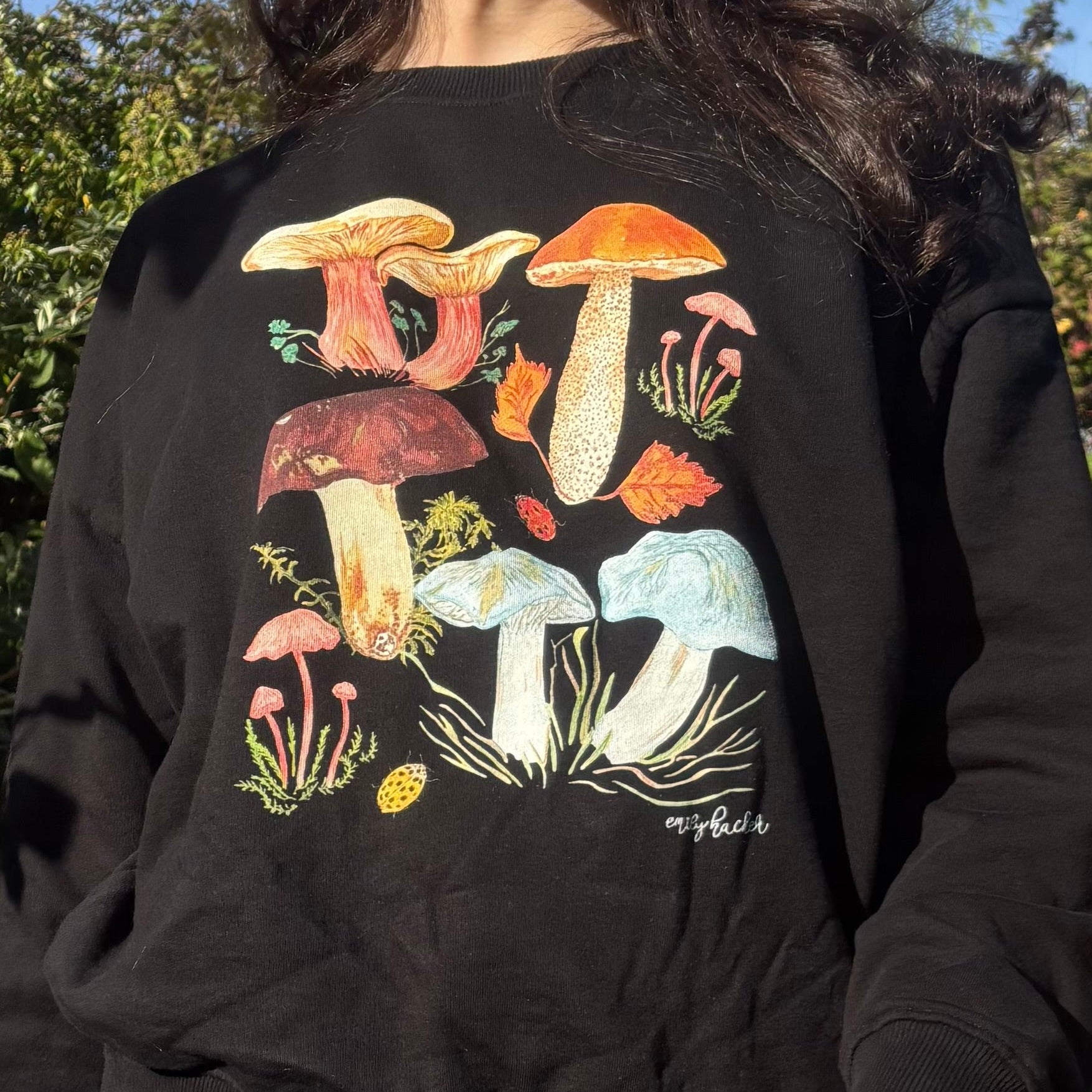 Person wearing a organic cotton black sweatshirt with colorful mushroom design outdoors