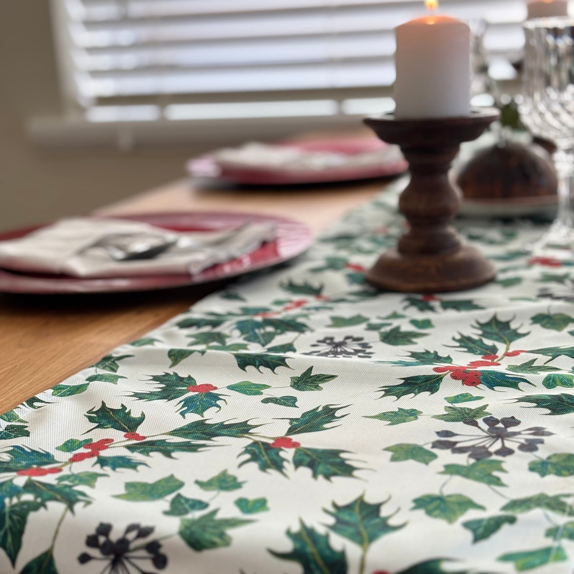 Christmas-themed table runner with holly design on a table setting.