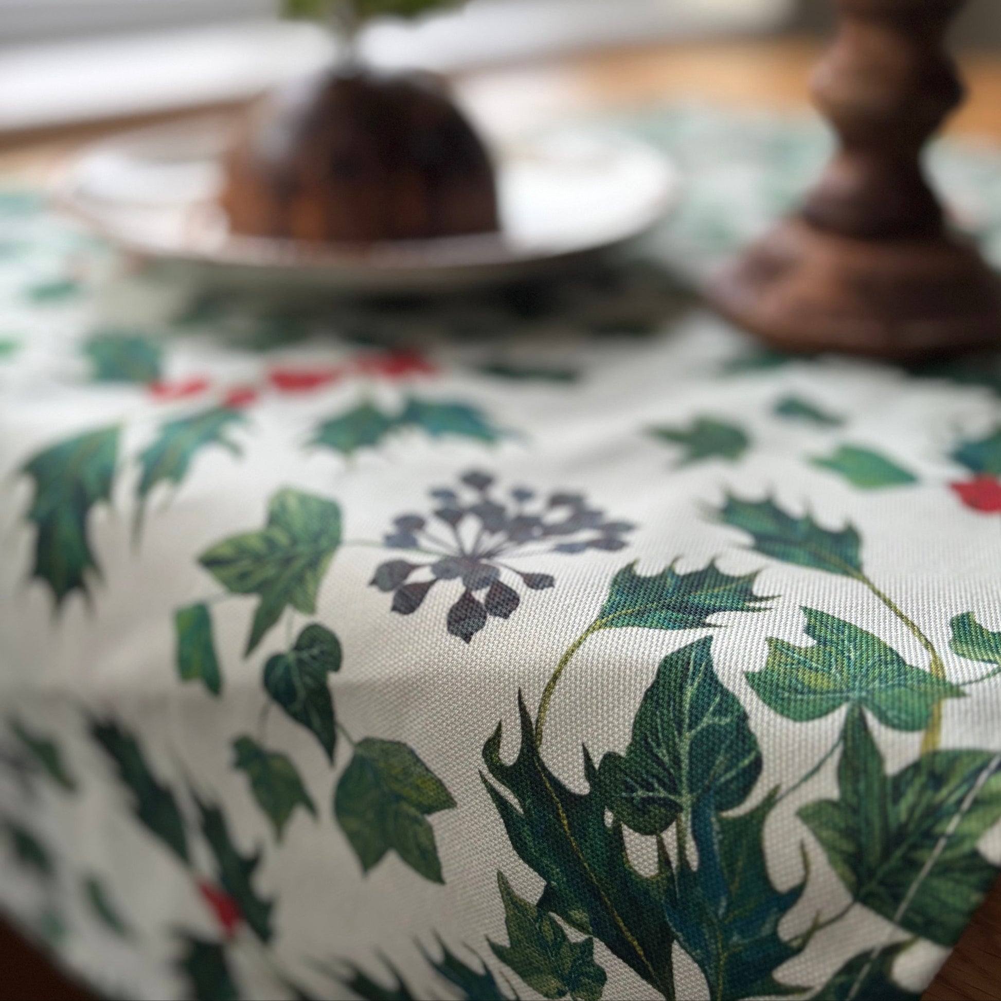Holly leaf and ivy pattern on a table setting with a wooden candle holder and dish.