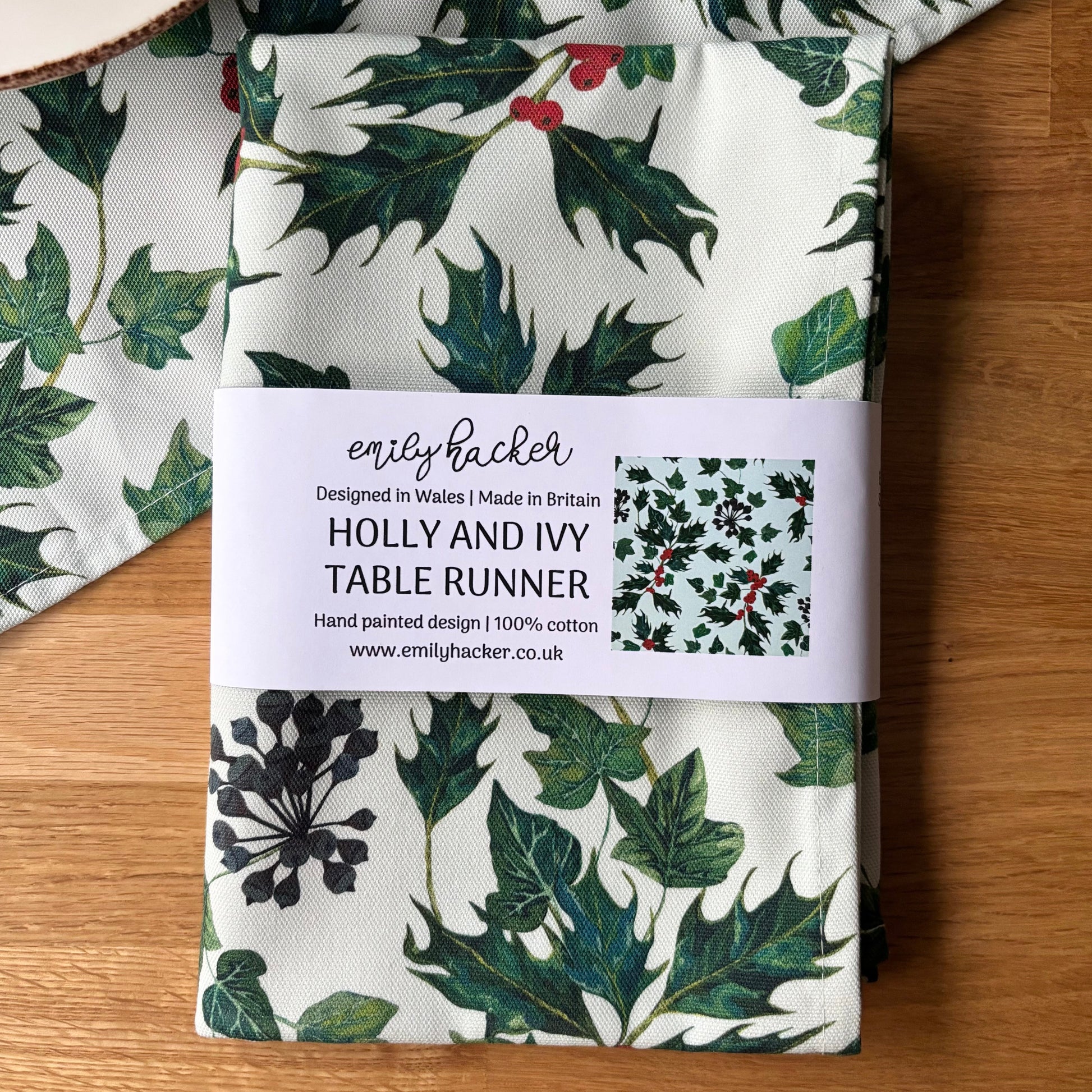Holly and ivy patterned table runner with a label on a wooden surface