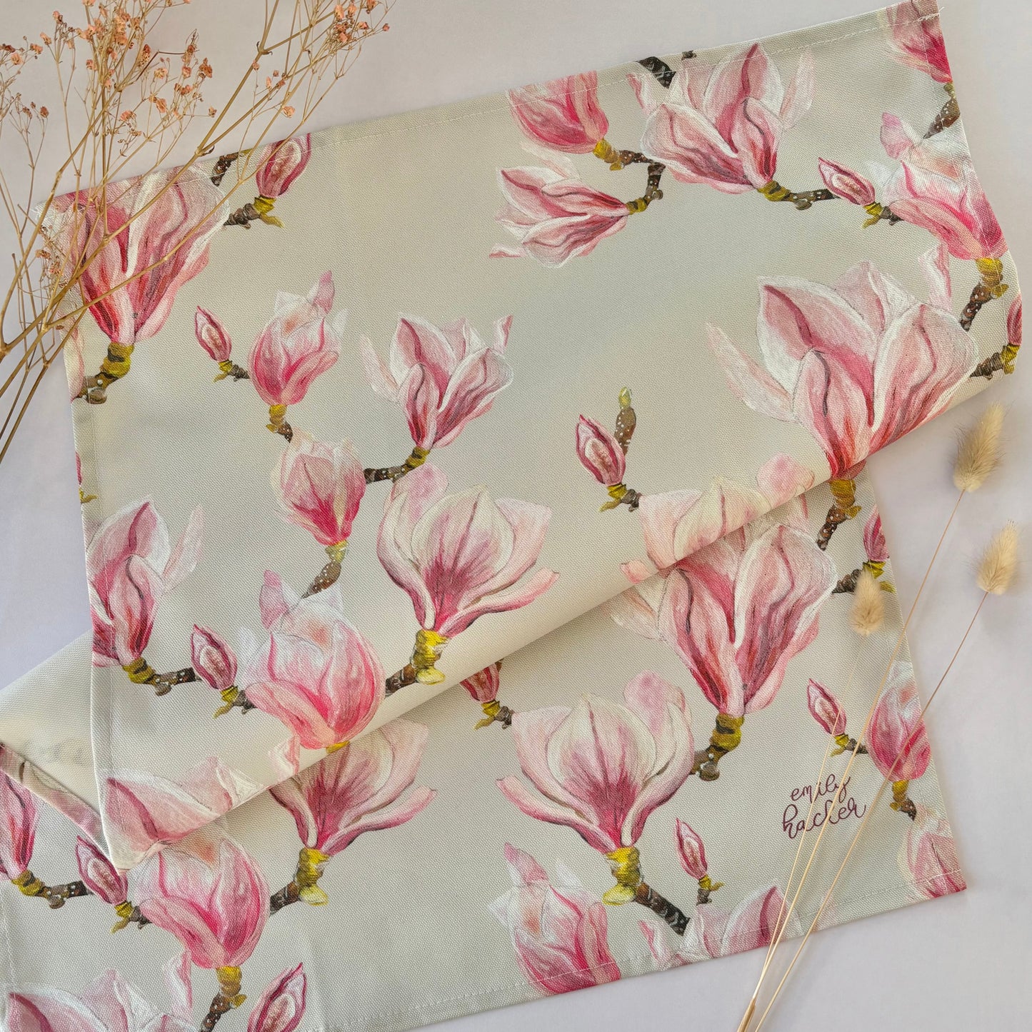 Floral patterned tea towel with pink magnolia blossoms on a white surface