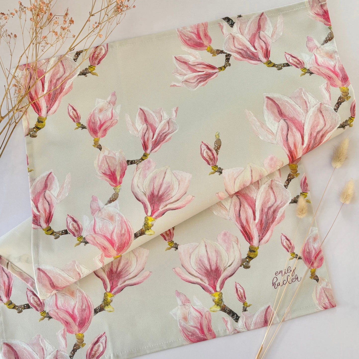 Floral patterned tea towel with pink magnolia blossoms on a white surface