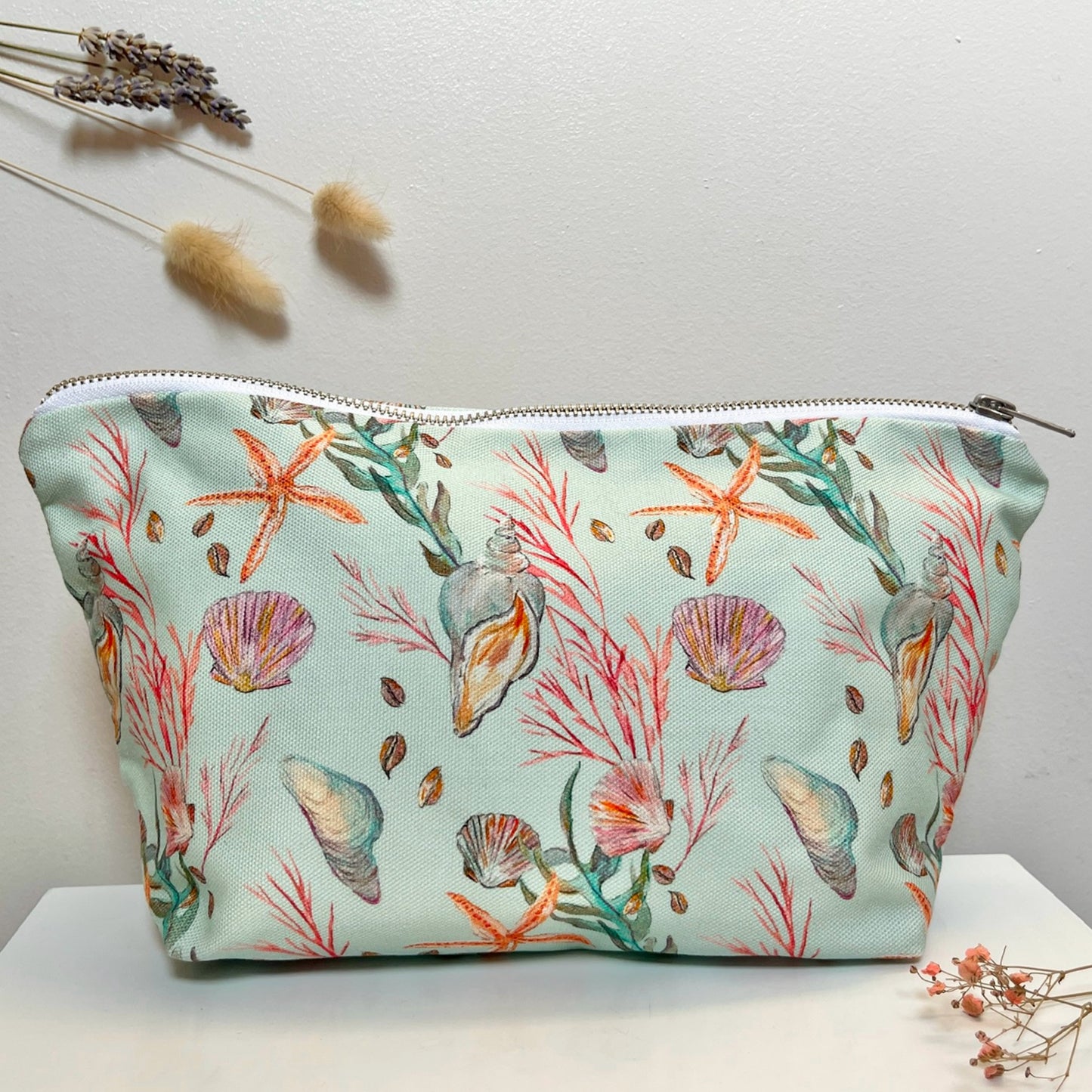 A light blue washbag with hand painted sea themed motifs including starfish, shells, and seaweed, displayed against a neutral background.
