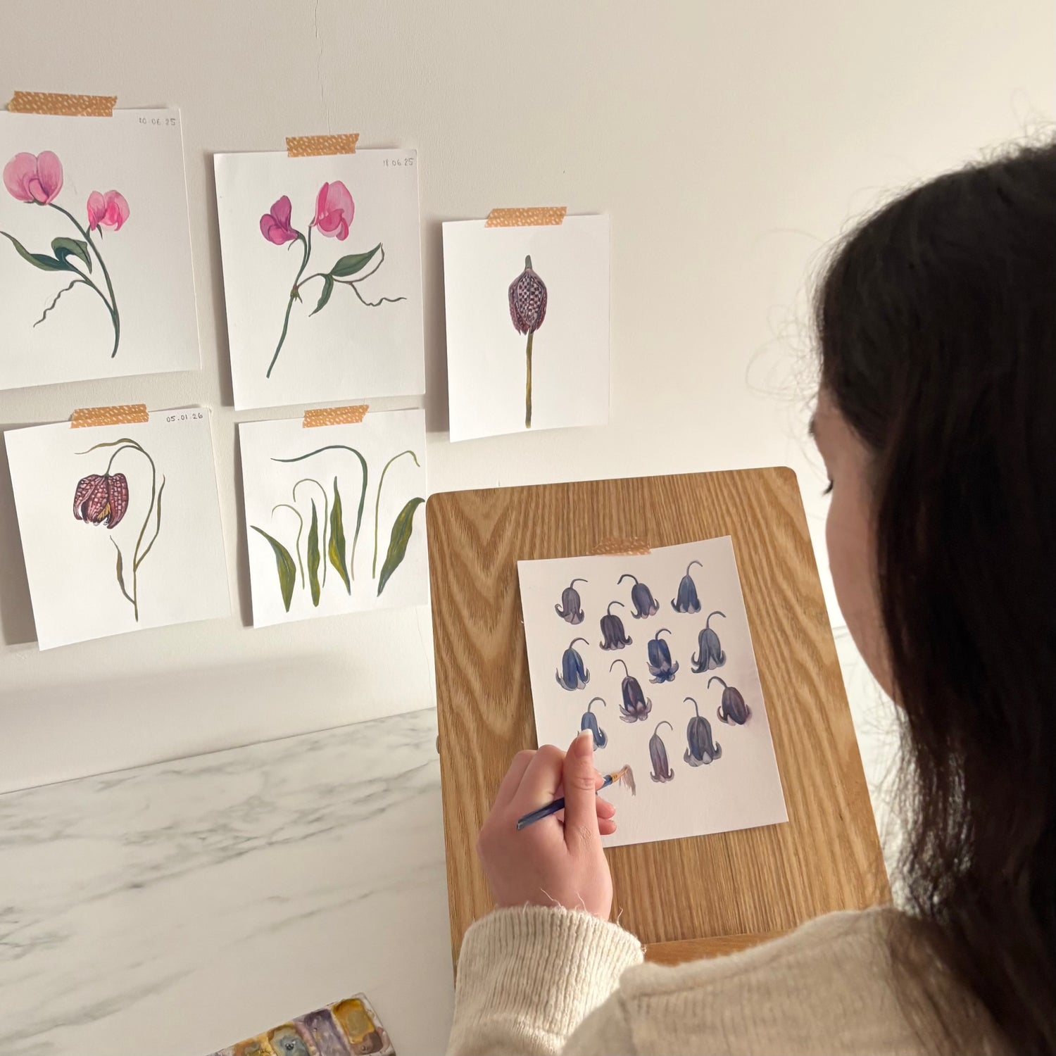 Studio picture with me painting  small flower illustrations on a piece of paper with floral artwork in the background.