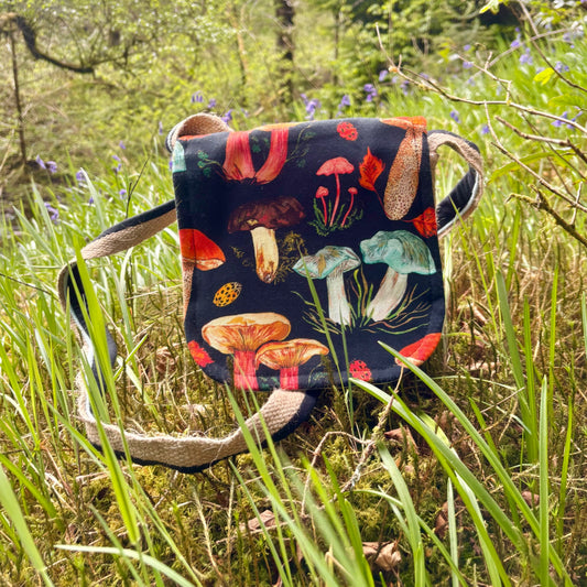 Handmade shoulder bag made from recycled bean sacks and illustrated mushroom fabric designed by store owner Emily. The bag is sat amongst a patch of bluebells