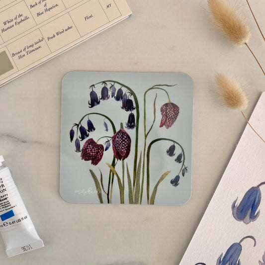 Coaster with floral English bluebell and snake head  design on a marble surface with art supplies.