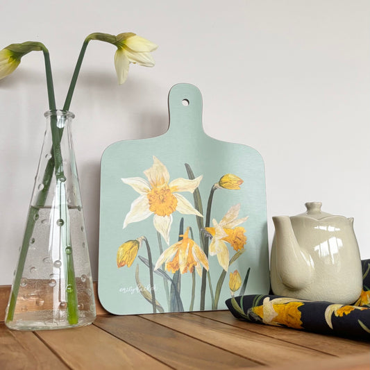 Daffodil Teal cutting board with floral wildflower design on a wooden surface with a vase and teapot.