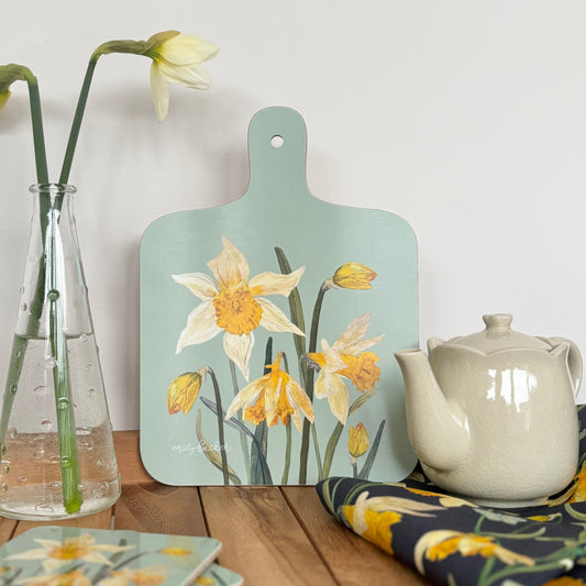 Daffodil Decorative cutting board with wildflower floral design on a wooden table with teapot and vase.