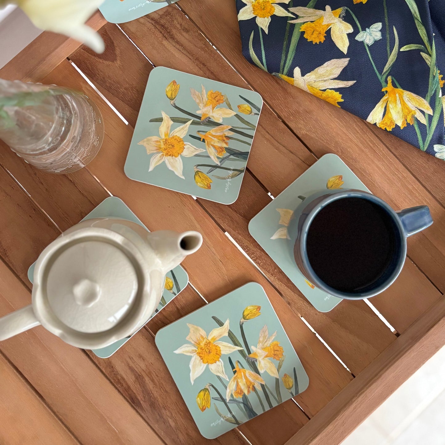 Set of floral coasters on a wooden table with a teapot and mug.